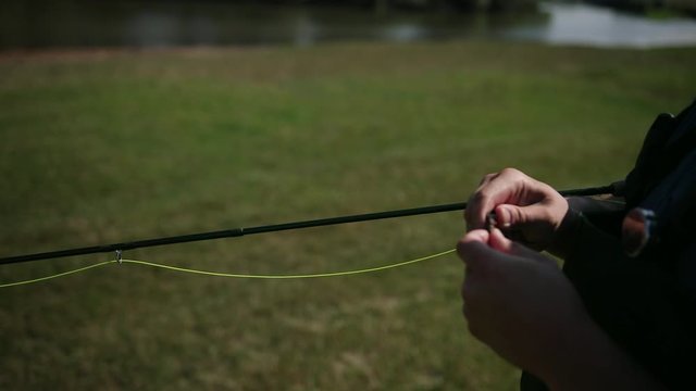 man fisherman, fishing, holding a fishing rod, stringing bait, spinning reel, on the street, by the river, standing on the shore on the green grass, Sunny weather, blue sky, summer, close-up
