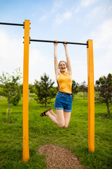Fototapeta premium Beautiful young woman hanging on the horizontal bar.