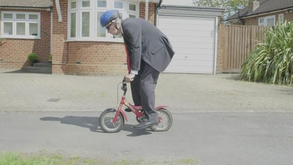Steady cam view of a caucasian businessman cycling on a child's bike themes of contrasts carefree humour young at heart