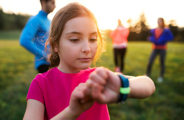 A portrait of small girl with large group of people doing exercise in nature.