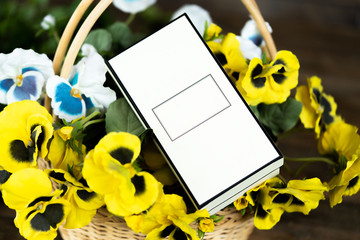 Close up of blank white box in basket with flowers on wooden table.