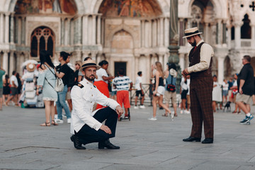 Two young men in vintage suits stand on Piazza San Marco square in Venice, Italy