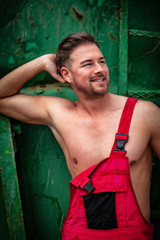 Porträt eines Hemdlosen lächelnden Mannes, der mit seiner aufgeknöpften Arbeitshose Muskeln zeigt