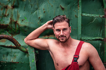 Porträt eines Hemdlosen lächelnden Mannes, der mit seiner aufgeknöpften Arbeitshose Muskeln zeigt