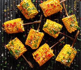 Grilled corn on the cob with butter, herbs, salt and aromatic spices on the grill plate, top view