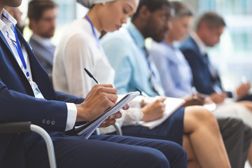 Businessman writing on notepad during seminar