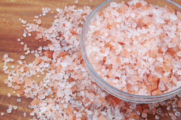 Pink rock salt in bowl and on wooden table
