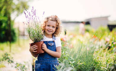 Portrait of small girl standing in the backyard garden, holding a plant in a pot.