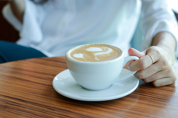 Asian girls hold a cup of white coffee and have a white heart-shaped cream on top.