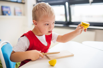 A down-syndrome school boy sitting at the desk in the classroom, learning.