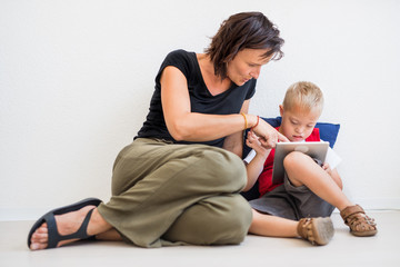 A down-syndrome school boy sitting on the floor with teacher, using tablet.