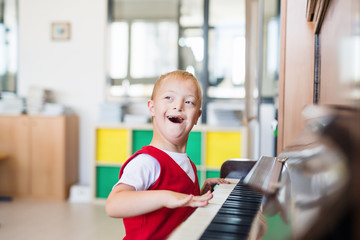 A down-syndrome school boy sitting at school, playing piano.
