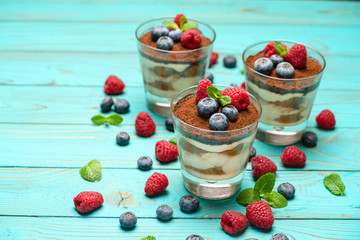 Classic tiramisu dessert with blueberries and strawberries in a glass cup on wooden background