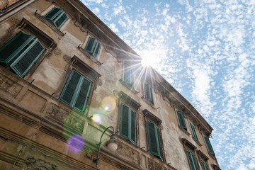 Italian renaissance windows with shutters. Sun flair and blue sky. Ferrara, Italy.