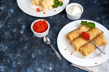 Pancakes stuffed with salted cottage cheese. In the bowl and spoon are red caviar and sour cream. Decorated with mint leaves.  