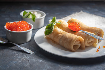 Pancakes stuffed with salted cottage cheese. In the bowl and spoon are red caviar and sour cream. Decorated with mint leaves.  