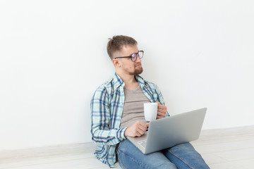 Positive young man in casual clothes and glasses surfing the Internet using Wi-Fi and a laptop in search of rental housing. Housewarming and apartment search concept.