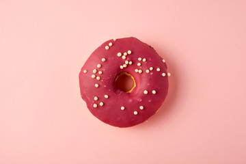 red round donut with white sprinkles on a pink background
