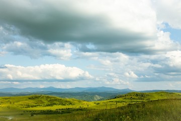 Hills with green grass and blue sky with white puffy clouds