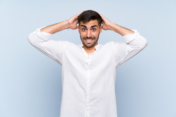 Handsome man with beard over isolated blue background frustrated and takes hands on head