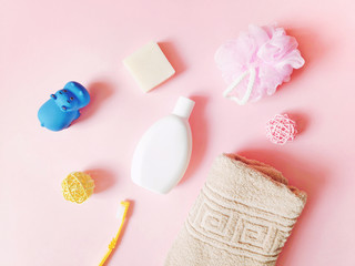 Flat lay photo baby care products on a pink background. Shampoo, soap, toothbrush, beige towel and rubber toy hippo