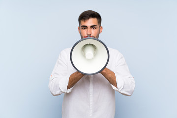 Handsome man with beard over isolated blue background shouting through a megaphone