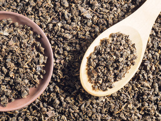 Background from fermented granulated tea from Cherry (Cerasus) leaves with spoon and clay plate