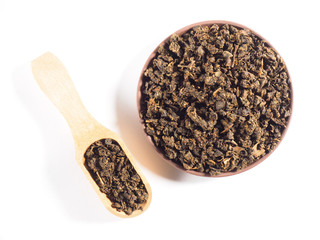 Fermented granular tea from Cherry (Cerasus) leaves on clay plate with wooden scoop on white background