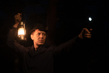 Detective agent with gun and kerosene lamp in night park.