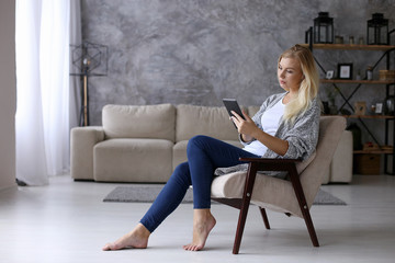 A girl sits in a chair in the morning and reads a tablet. Comfortably working remotely at home. Copy space.