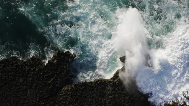 Top aerial slow motion view of rocky cliff, beautiful azure ocean and high waves crashing with great splashing and white foam. Bali, Indonesia