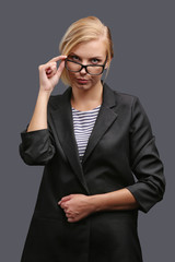 Woman, a teacher in a jacket and glasses on a gray background, expresses emotions. Copy space.