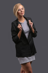 Woman, a teacher in a jacket and glasses on a gray background, expresses emotions. Copy space.