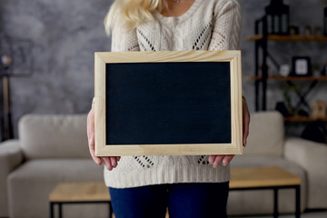 Girl holds a chalk board in the apartment. Copy space.