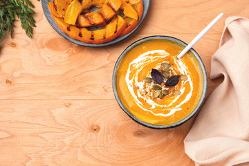 Pumpkin soup in a plate on a wooden background, top view. Slices of grilled pumpkin. Copy space.