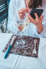 woman with glass of wine sitting in restaurant looking into phone