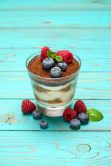 Classic tiramisu dessert with blueberries and strawberries in a glass cup on wooden background