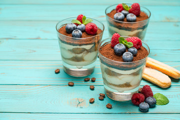 Classic tiramisu dessert with blueberries and strawberries in a glass cup and savoiardi cookies on wooden background