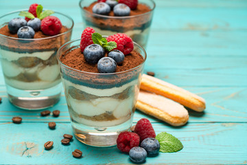 Classic tiramisu dessert with blueberries and strawberries in a glass cup and savoiardi cookies on wooden background
