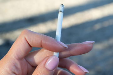 Slim cigarette in a female hand with a pink manicure