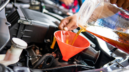 Auto mechanic hand pouring and replacing fresh oil into car engine at auto repair garage....