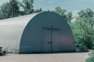 Fototapeta na wymiar Large gray hangar among the trees