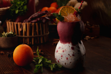 orange cocktail in a tiki glass on a wooden background. Background decorated with fruits and herbs.