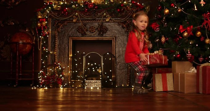 A pretty little girl takes off the Christmas cap in apartment with christmas lights and decorations. Merry Christmas, happy New Year. Miracle time.