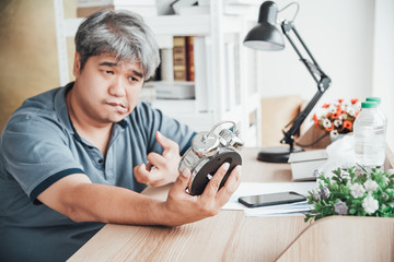 Blurred of Asian man, He is patient from neurological diseases, or hemiplegia having a facial palsy and kinking fingers, He is looking at the alarm clock in his hand, to health and paralysis concept. - obrazy, fototapety, plakaty
