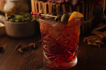 cocktail in rox decorated with black olives on a wooden background. Background decorated with fruits and herbs.