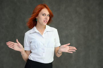 Photo Portrait of a cute girl woman with bright red hair manager in a white shirt on a gray background in the studio. He talks, shows his hands in front of the camera with emotions.