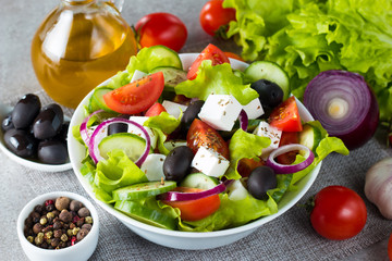 Fresh Greek salad made of cherry tomato, ruccola, arugula, feta, olives, cucumbers, onion and spices. Caesar salad in a white bowl on wooden background. Healthy organic diet food concept.