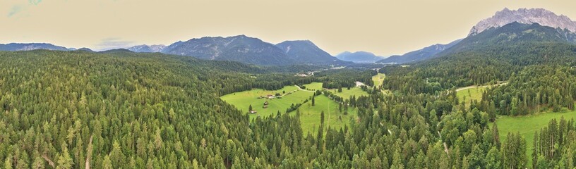 Obraz premium Panorama of a forest and a valley with meadows and pastures in front of the mountains of the Alps, composed of several aerial photos, high resolution