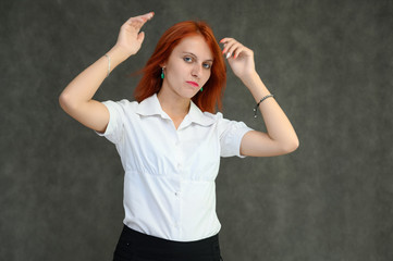 Photo Portrait of a cute girl woman with bright red hair manager in a white shirt on a gray background in the studio. He talks, shows his hands in front of the camera with emotions.